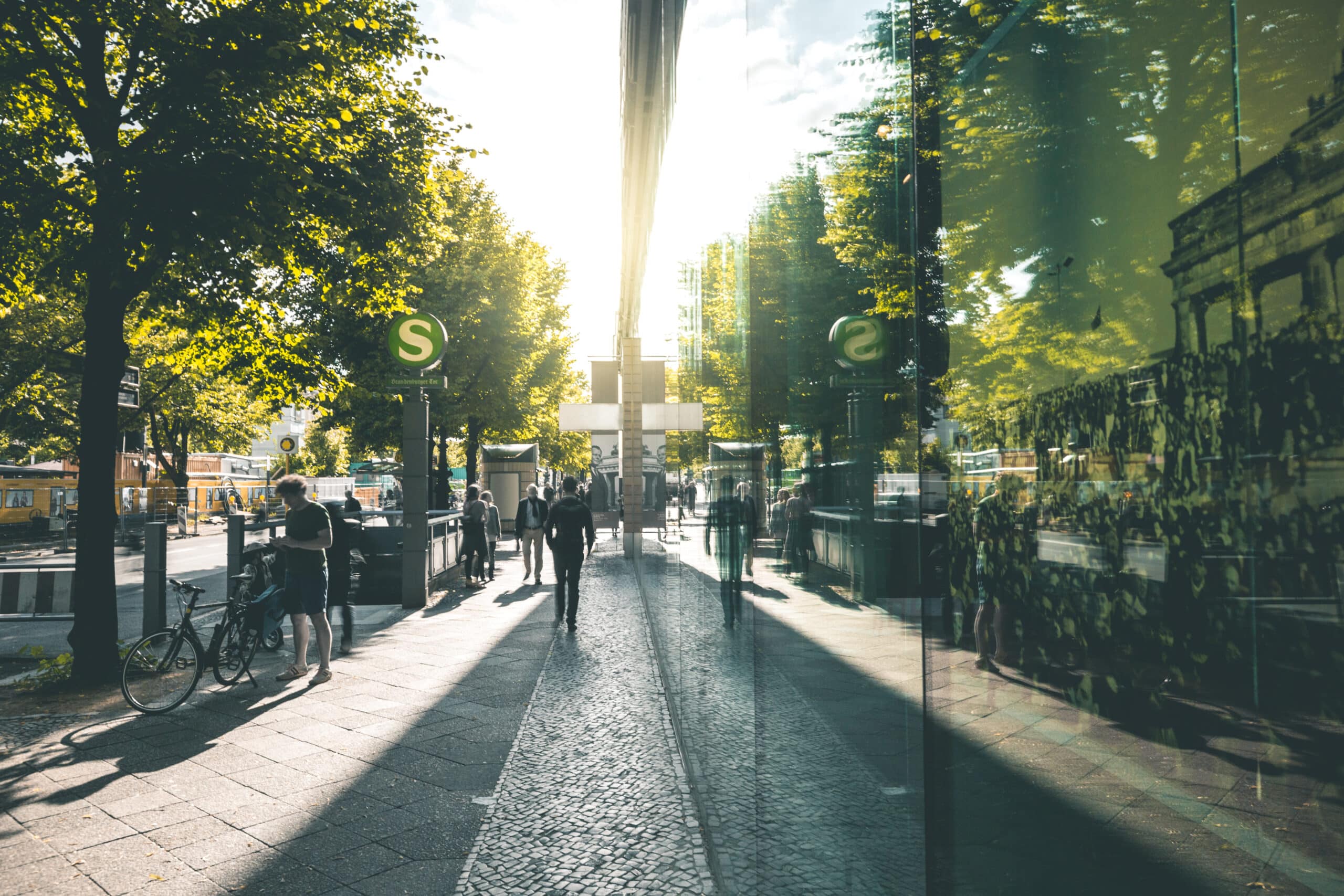 People walking along a modern street with green trees and shining sun